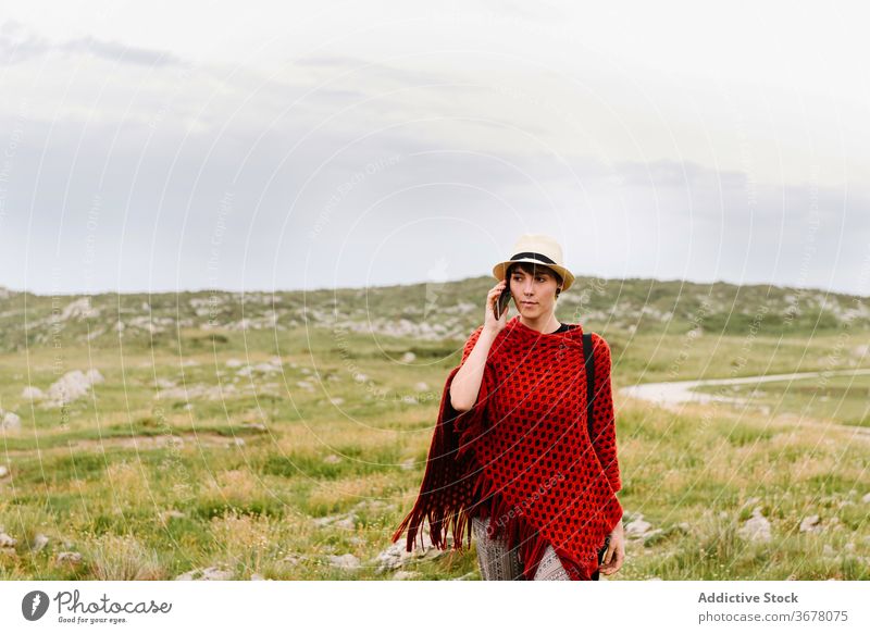 Stilvolle Frau spricht auf Smartphone in der Natur reisen reden Telefon Anruf trendy Mobile Narren von Arenillas Spanien Asturien llanes Poncho Strickwaren rot