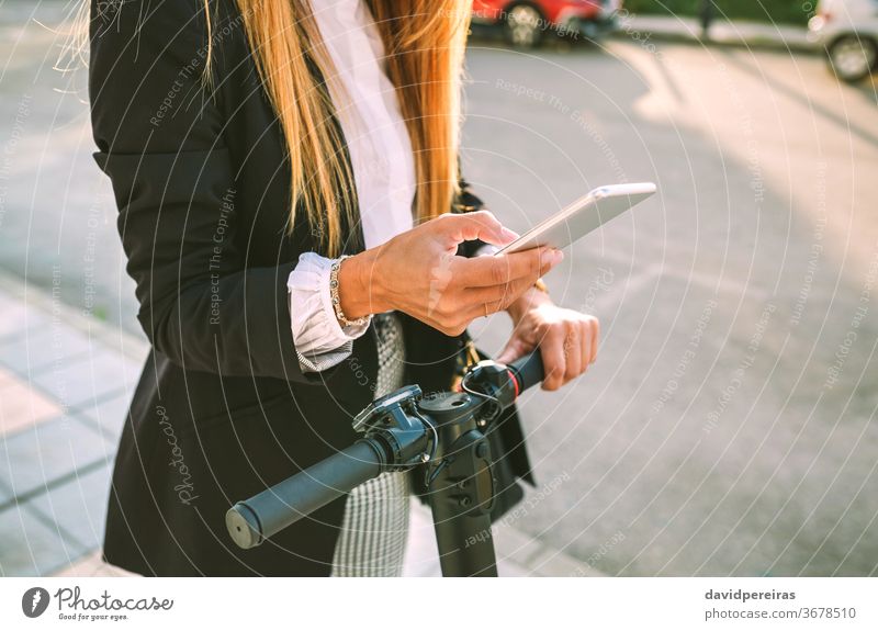 Nicht erkennbare Geschäftsfrau mit E-Scooter beim Blick auf das Handy urban unkenntlich Texten Funktelefon Tretroller Großstadt Frau Straße Mode Mobile Arbeiter