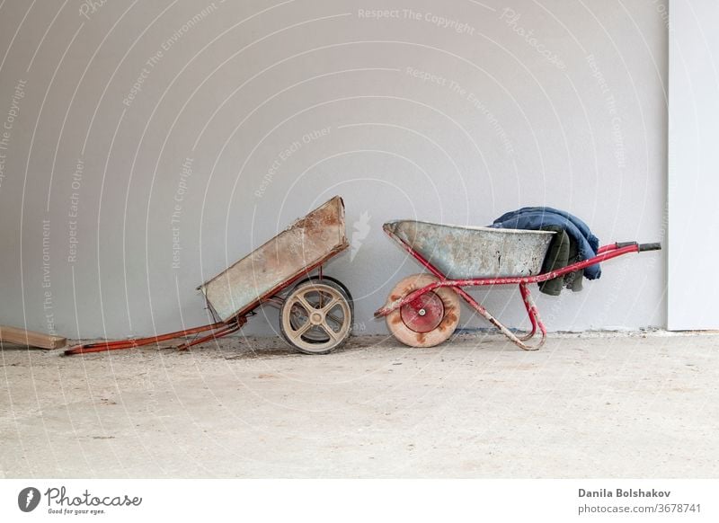 alter Bauwagen und Schubkarre auf dem Hintergrund einer Stuckwand Container retro Einzelrad altehrwürdig Gartenarbeit Metall Industrie Werkzeuge Maschinenbau