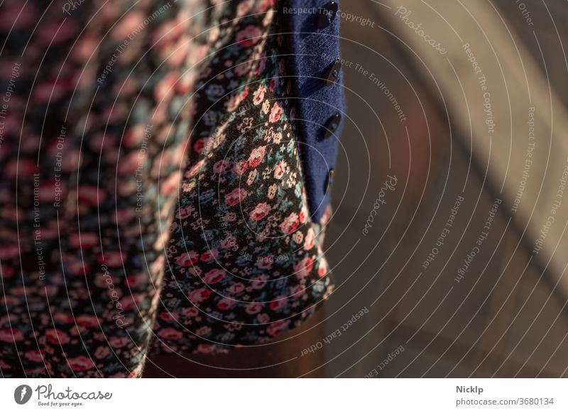 eine junge Frau trägt einen schwarzen Rock mit Blumenmuster und eine blaue Strickjacke mit schwarzen Knöpfen - Detailaufnahme - Abendsonne - Lichtstimmung