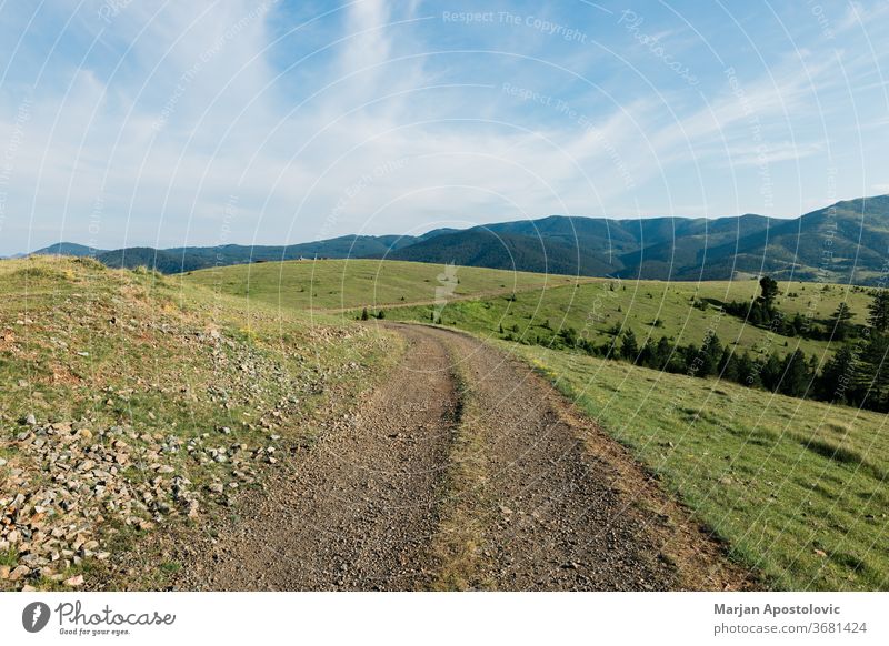 Unbefestigte Straße in den Bergen an einem sonnigen Tag Hintergrund schön blau Wolken Land Landschaft Schmutz Umwelt erkundend Feld Gras grün wandern Hügel