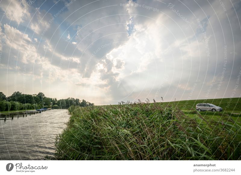 Kanal mit Schilf im Gegenlicht hinter dem Ijsselmeerdeich Wasser Wolkenhimmel Gegnlicht Lichtstrahlen godrays Farbfoto Menschenleer Außenaufnahme Himmel Tag