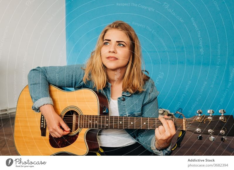 Nachdenkliche Frau spielt Gitarre auf dem Boden spielen nachdenklich Musiker Stock Wand akustisch jung lässig Instrument sitzen Gesang Melodie Denken besinnlich