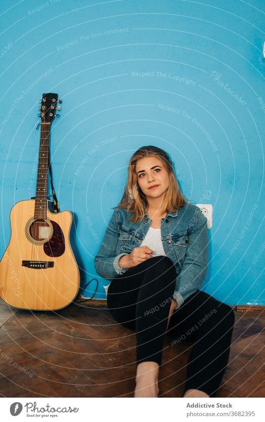 Nachdenkliche Frau sitzt in der Nähe von Gitarre auf dem Boden spielen nachdenklich Musiker Stock Wand akustisch jung lässig Instrument sitzen Gesang Melodie