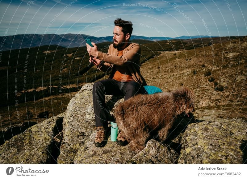 Bärtiger Reisender mit Hund benutzt Smartphone in den Bergen Mann Berge u. Gebirge benutzend Stein sitzen navigieren puerto de la morcuera Spanien männlich