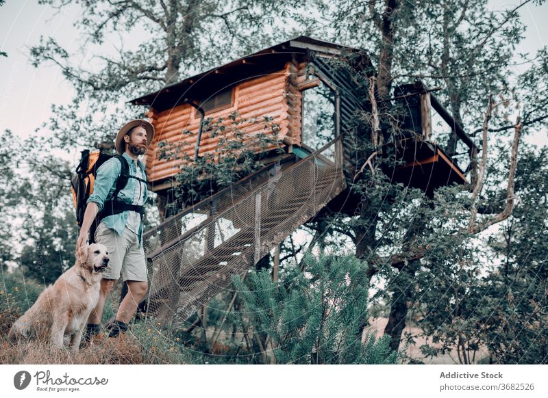 Reisender Mann in der Nähe von Baumhaus mit Hund im Wald Haus Kabine Hütte Rucksack Wälder hölzern Gebäude Abenteuer männlich reisen Tourismus Natur Feiertag