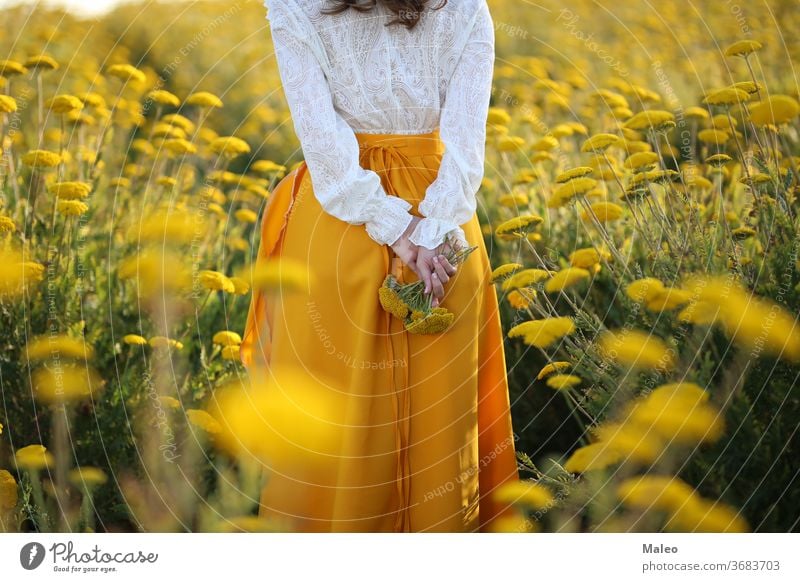 Ein Mädchen in einem gelben Rock und einer weißen Bluse steht in einem Feld gelber Blumen Hintergrund böhmen Land Paar Abenddämmerung Finger Gras grün Höhe