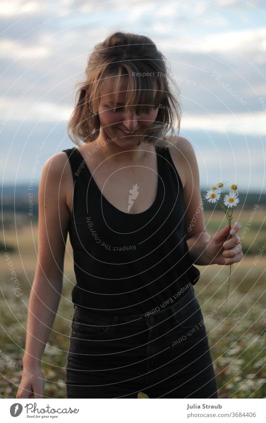 Junge Frau mit Kamillenblüten in der hand blond brünett schwarz Top Jeanshose ponyfrisur Kurzhaarschnitt Blumenfeld kamillenfeld lächelnd lächelnde Frau Wolken