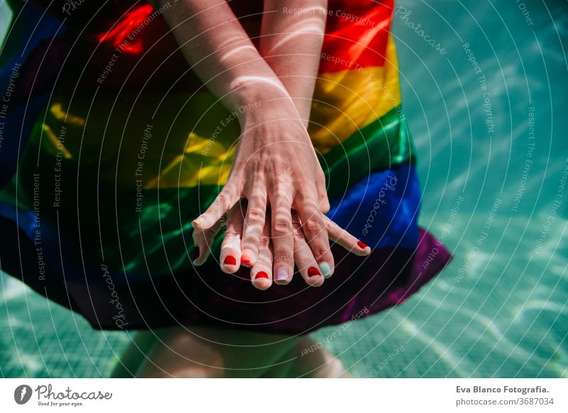 zwei Frauen am Pool zusammen mit einer regenbogenfarbigen Schwulenfahne umwickelt. LGBT-Konzept Liebe lesbisch Schwulenflagge unter Wasser Schwimmbad