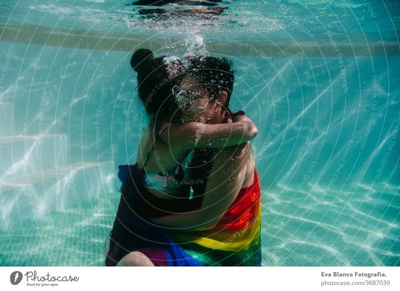 zwei Frauen am Pool zusammen mit einer regenbogenfarbigen Schwulenfahne umwickelt. LGBT-Konzept Liebe lesbisch Schwulenflagge unter Wasser Schwimmbad