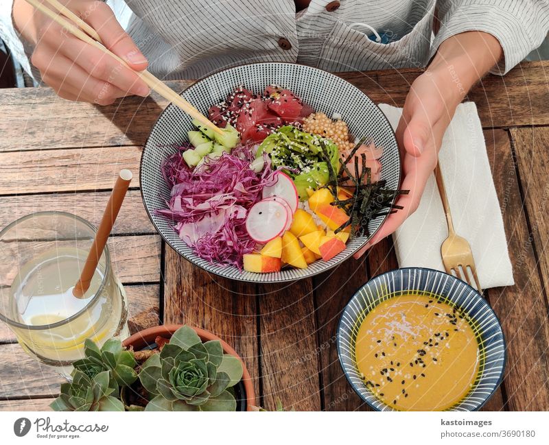 Frau isst schmackhafte, farbenfrohe, gesunde, natürliche, biologisch-vegetarische, hawaiianische Stocherschüssel mit asiatischen Essstäbchen auf einem rustikalen Holztisch. Gesundes, natürliches, organisches Esskonzept.