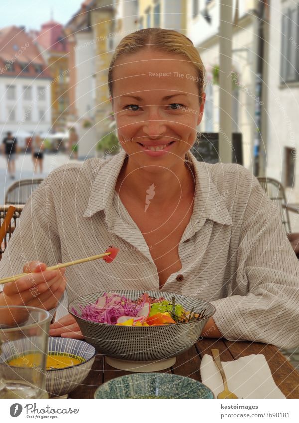 Frau isst schmackhafte, farbenfrohe, gesunde, natürliche, biologisch-vegetarische, hawaiianische Stocherschüssel mit asiatischen Essstäbchen auf einem rustikalen Holztisch. Gesundes, natürliches, organisches Esskonzept.