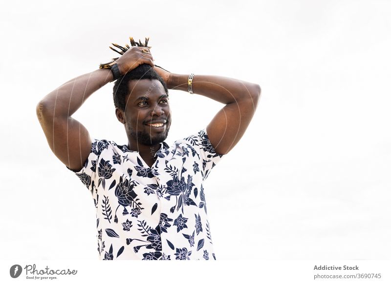 lächelnder schwarzer Mann, der sein Haar in einem Schwanz hält Afrikanisch Behaarung männlich jung Amerikaner Afro-Look berührend Typ Glück gutaussehend Blick