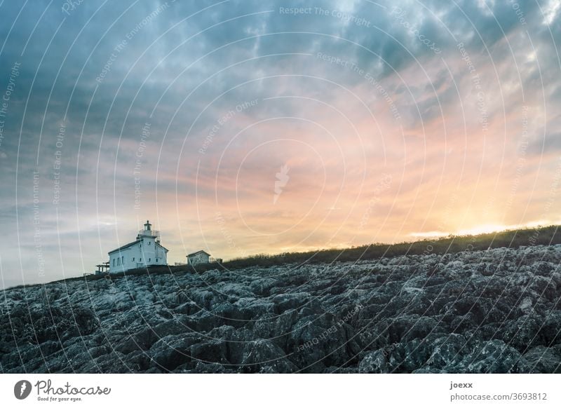 Kleines Haus mit Leuchtturm vor Himmel bei Sonnenuntergang Landschaft Idylle Ruhe Horizont Meer orange felsküste Küste Felsen Sonnenuntrgang Farbfoto