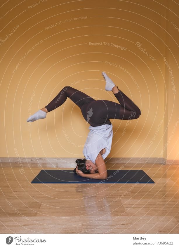 anonyme Frau beginnt unterstützte Kopfstand-Pose. Seitenansicht einer schlanken Frau, die tagsüber zu Hause in einem gemütlichen Wohnzimmer Yoga macht. Mädchen