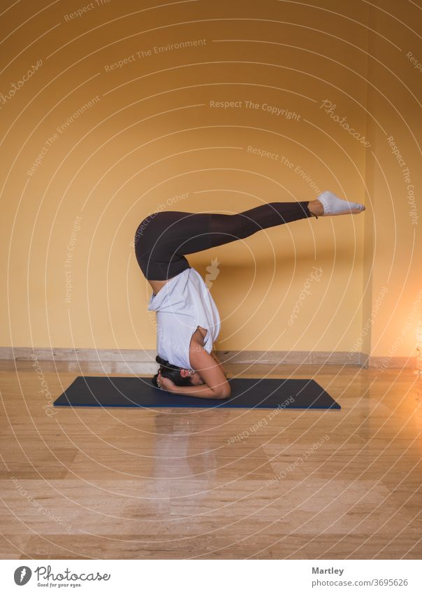 anonyme Frau beginnt unterstützte Kopfstand-Pose. Seitenansicht einer schlanken Frau, die tagsüber zu Hause in einem gemütlichen Wohnzimmer Yoga macht. Mädchen