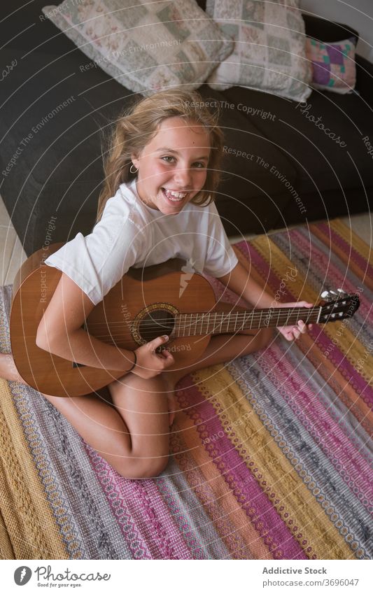 Mädchen sitzt auf dem Boden spielen eine Gitarre, während ist lächelnd und mit Blick auf die Kamera vertikal Musik Künstler Klassik Lernen Musiker Spielen üben