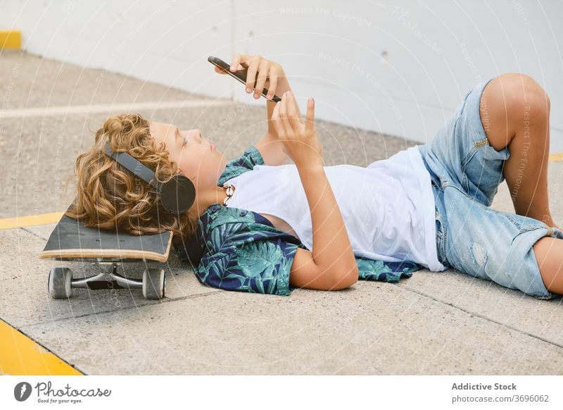 Junge auf dem Boden liegend mit einem Skateboard, der Musik hört und auf sein Handy schaut Jugendzeit zuhören Einsamkeit Gesang Stilrichtung Generation Teenager