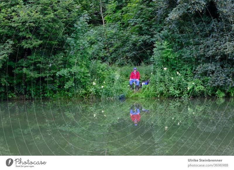 Angler sitzt am Flussufer im Grünen Angeln Wasser Fischer Ansitzen Ufer Gebüsch Wald grün Geheimplatz Erholung Stille Ruhe Fische fangen Freizeit & Hobby Natur