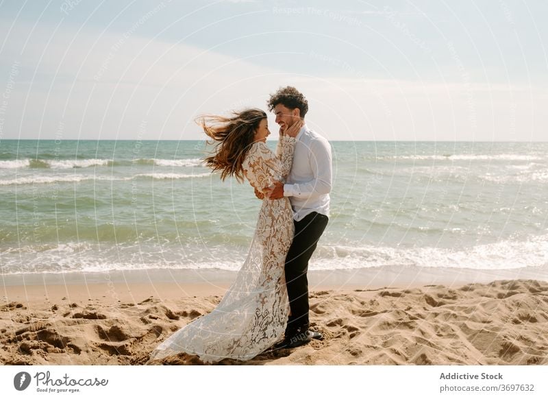 Glückliches frisch verheiratetes Paar steht gegen wogende Meer Jungvermählter Strand romantisch heiter Zusammensein Umarmen Partnerschaft MEER Liebe Natur Sand