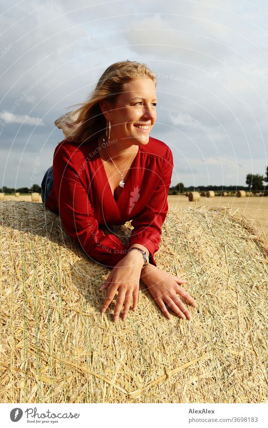 Junge Frau liegt auf einem Strohballen auf dem Feld und lächelt Freizeit Spaß Freude Jeans Ganzkörper Zentralperspektive Blick in die Kamera