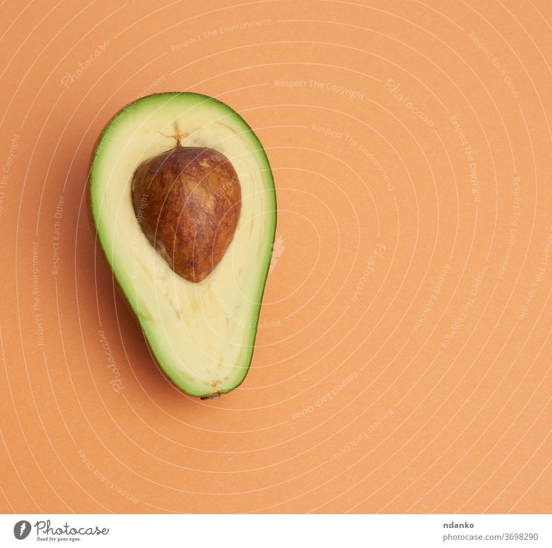 halbreife grüne Avocado mit braunen Knochen auf einem abstrakten orangefarbenen Hintergrund Nahaufnahme Farbe kreativ geschnitten lecker Diät Essen exotisch