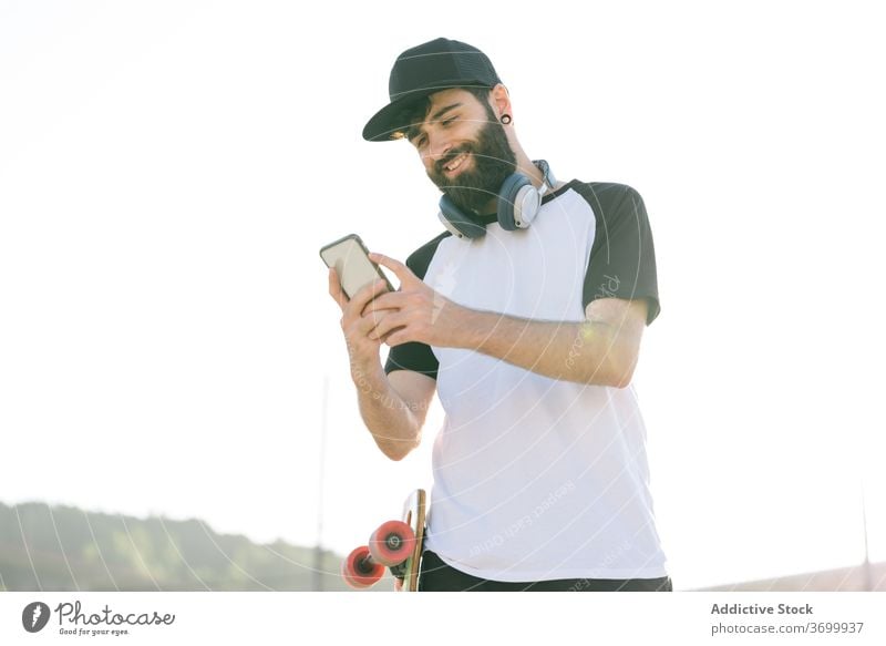 Sorgloser männlicher Skater, der in der Stadt auf seinem Handy surft Hipster Longboard Straße Mann Smartphone Wochenende genießen benutzend soziale Netzwerke