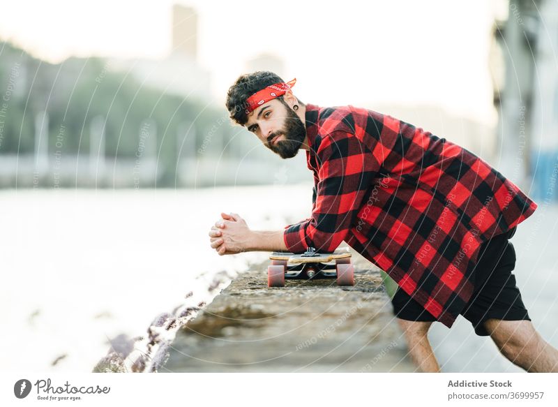 Hübscher Skater auf der Promenade in der Stadt Mann gutaussehend Longboard Großstadt Spazierweg kariertes Hemd Hipster urban trendy männlich Stauanlage Stein