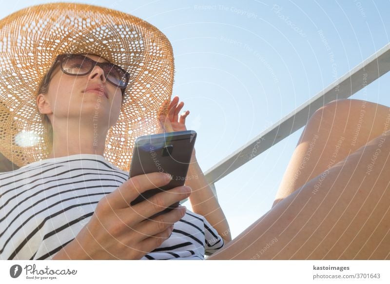 Schöne, romantische, blonde Frau in den Sommerferien, die mit einer Fähre auf einem Kreuzfahrtschiff reist und dabei ihr Mobiltelefon hält und benutzt. Lebensstil in den Sommerferien