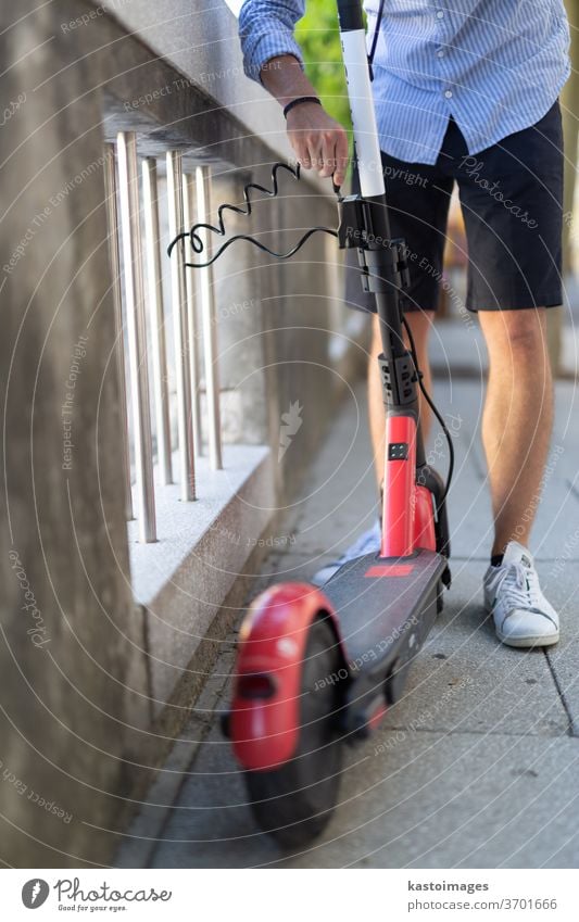 Männlicher Benutzer parkt Elektroroller sicher und verriegelt ihn an einem Zaun. Umweltfreundliches, grünes, modernes städtisches Mobilitätskonzept zur gemeinsamen Nutzung von Verkehrsmitteln mit Elektrorollern zur Miete in Ljubljana, Slowenien