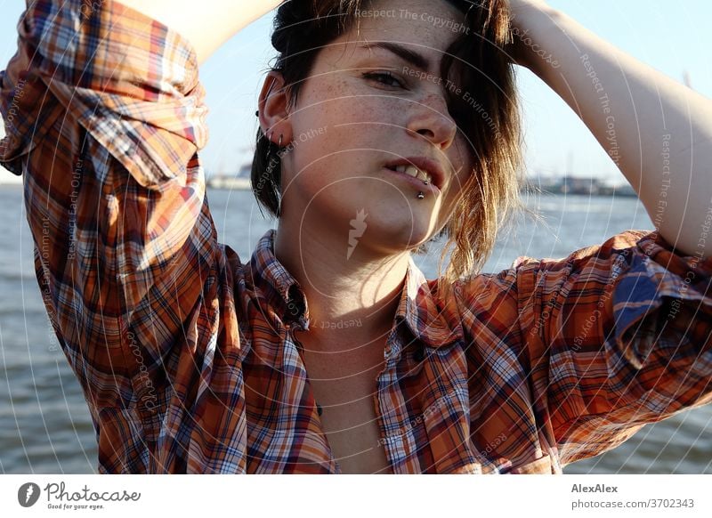 Junge Frau mit Sommersprossen sitzt auf einem Ponton vor Hamburger Hafen Porträt Zentralperspektive Blick brünettes Haar Textfreiraum rechts sommersprossig