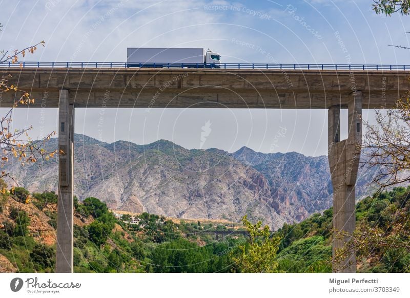 Lastwagen mit Kühlsattelanhänger überquert ein Viadukt mit einer Berglandschaft im Hintergrund Brücke Straße gekühlt Berge trayler Transport Verkehr Autobahn