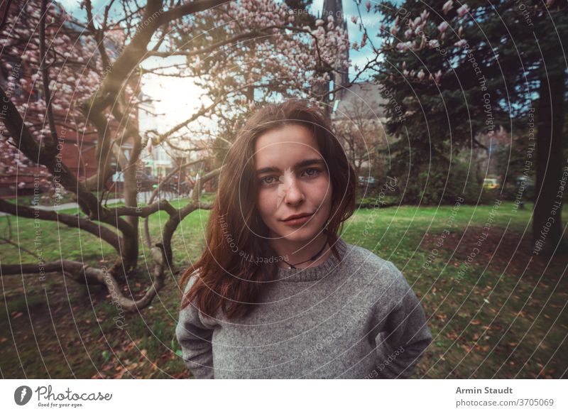 Porträt einer jungen, lächelnden Frau in einem Park vor einem Magnolienbaum im Freien Lächeln schön Natur Kirche Frühling Blüte glücklich froh Aussehen