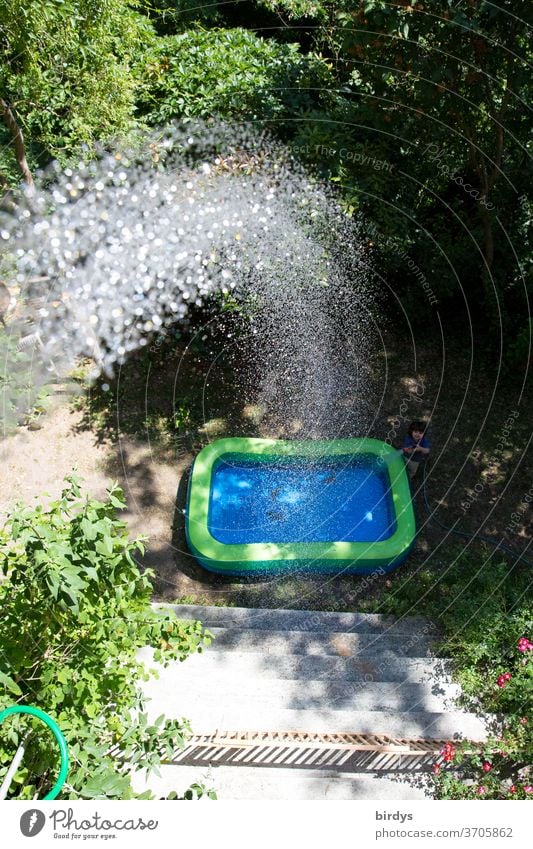 Ein Planschbecken im Garten das vom Balkon aus befüllt wird.  Wasserstrahl Sommer Hitze Abkühlung Wassertropfen Erfrischung Sonnenlicht Freude Vogelperspektive