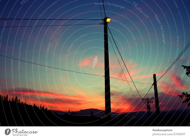 Pfahlmast Silhouette einer leuchtende Straßenlaterne im Dämmerlicht eines schillernden Sonnenuntergangs Himmel Mast Laternenmast Straßenlaternen Lampe