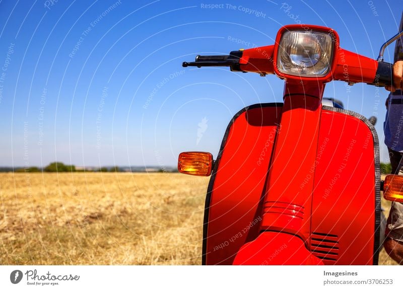 klassischer Roller auf einem weitläufigen Feld mit trocknendem Gras in der Hitze des Sommers mit Kopierraum links Motorroller Transport Retro-Stil Motorrad