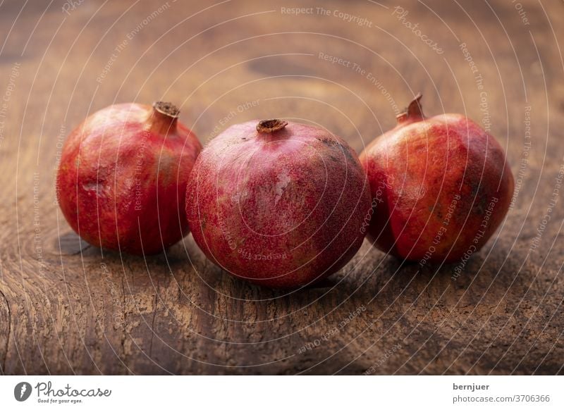 drei Granatäpfel auf dunklem Holz Granatapfel rustikal Hintergrund Obst saftig weiß Essen tropisch exotisch rot süß granatum natürlich Dessert geschnitten