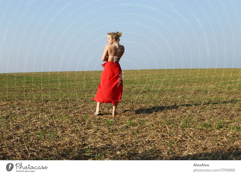 Portrait in Hinteransicht einer jungen Frau mit Bikini- Top und rotem Rock auf einem Feld Licht sportlich feminin Gefühle emotional Porträt Zentralperspektive