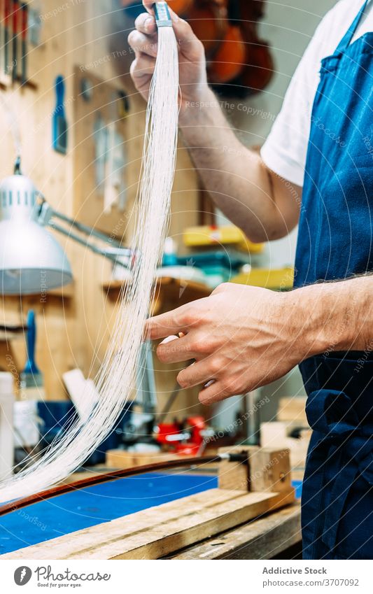 Anonymer Handwerker bei der Arbeit mit Bogenhaar für Musikinstrument Zupfinstrumentenmacher Behaarung Schleife Reparatur Kunstgewerbler wiederherstellen Mann