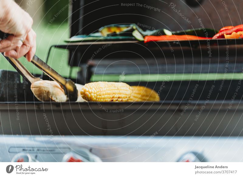 eine Person steht am Grill mit Grillzange und Gemüse Mann Frau grillen Mais Brot Zucchini Lebensmittel Fleisch Grillrost Ernährung Grillsaison lecker Abendessen