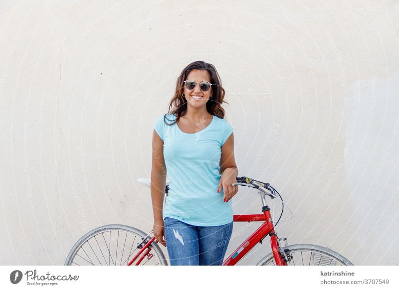 Junge Frauen mit Fahrrad bleiben in der Nähe einer Mauer jung Mädchen anhaben Attrappe T-Shirt Jeanshose Aufenthalt Wand Lächeln Rundhals Bekleidungsmockup