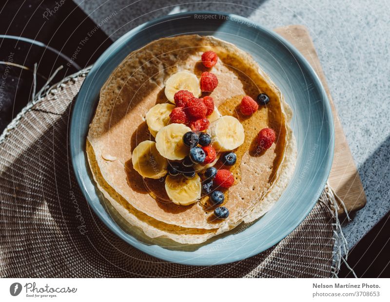 Überblick über eine köstliche Crêpe mit Bananen, Heidelbeeren, Himbeeren und Honig. Die Küche ist mit einem schönen natürlichen Licht beleuchtet. Lebensmittel