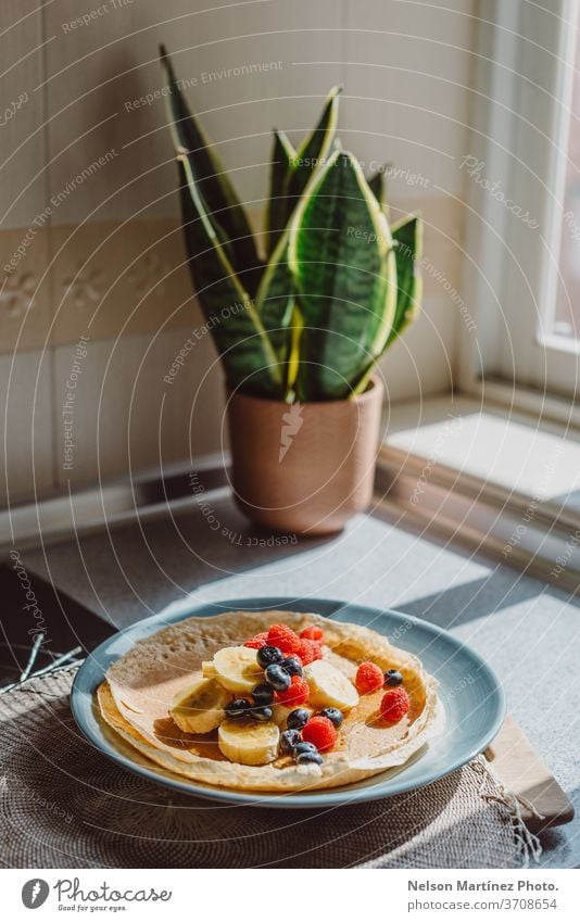 Köstlicher Crêpe mit Bananen, Heidelbeeren, Himbeeren und Honig. Die Küche ist mit einem schönen natürlichen Licht beleuchtet. Lebensmittel Dessert lecker süß