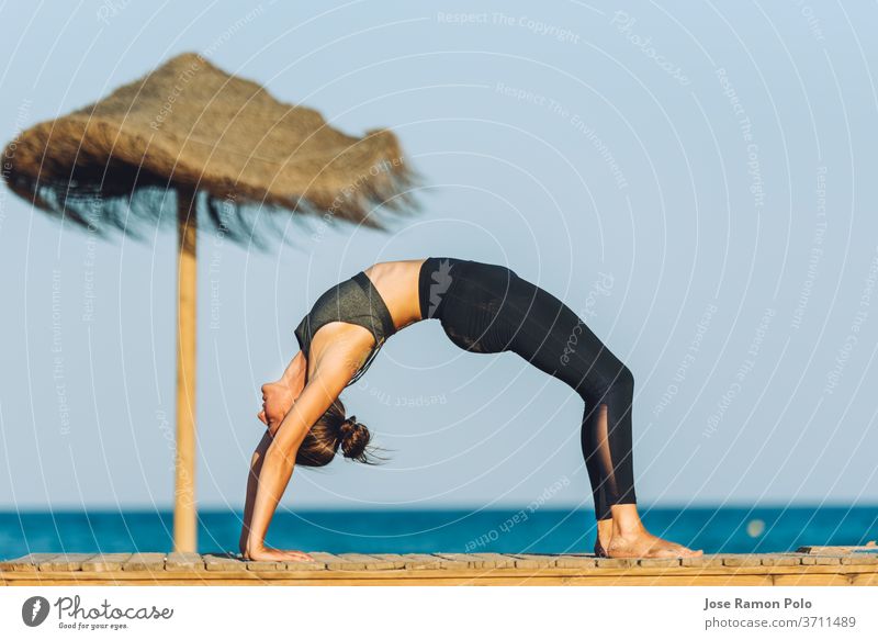 junge Frau bei einer Yoga-Brückenübung am Strand vor dem Meer neben einem Sonnenschirm auf Menschen Übung Meditation Person Sport Fitness Erholung Wellness