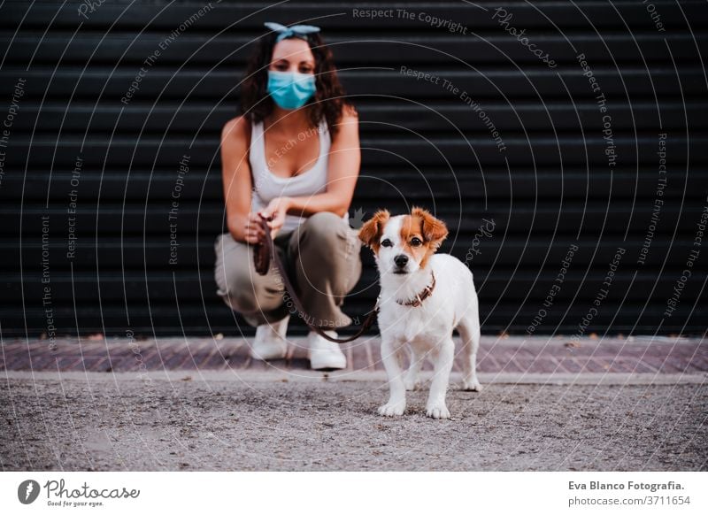 junge Frau im Freien mit Schutzmaske, daneben süßer Jack-Russell-Hund. Neues normales Konzept Straße neue Normale jack russell Haustier laufen urban Großstadt