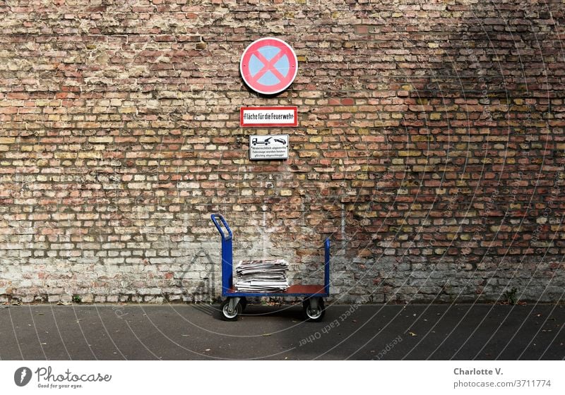 Im Halteverbot | Handwagen mit Zeitungen vor Ziegelwand mit Haltverbotsschild transportwagen zeitungen Zeitungsstapel Halteverbotsschild Feuerwehrfläche