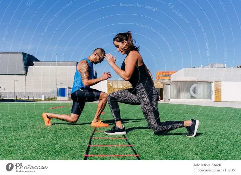 Athletisches Paar beim Training mit der Agility-Leiter auf dem Sportplatz Laufmasche Beweglichkeit Übung Gerät Ausfallschritt Zusammensein Fitness passen