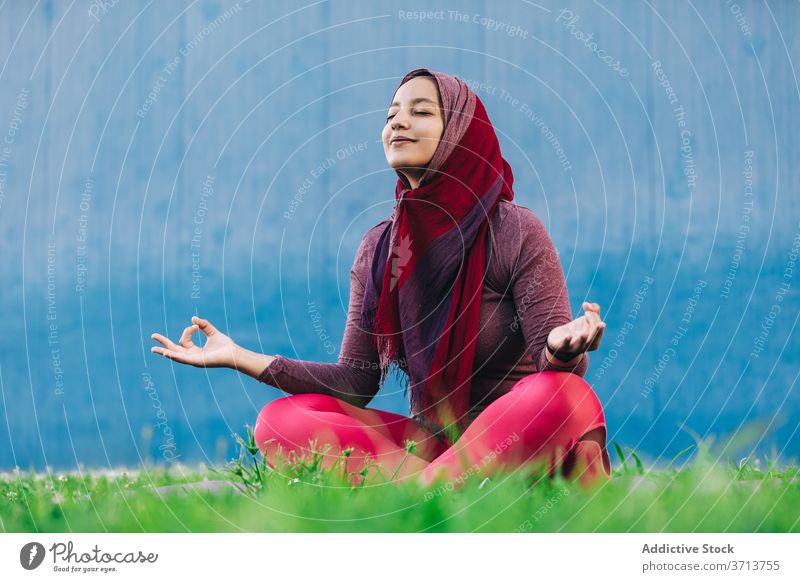 Muslimische Frau meditiert in Lotus-Pose meditieren Yoga Park üben Asana Achtsamkeit Stressabbau padmasana arabisch ethnisch Hijab muslimisch Sportbekleidung