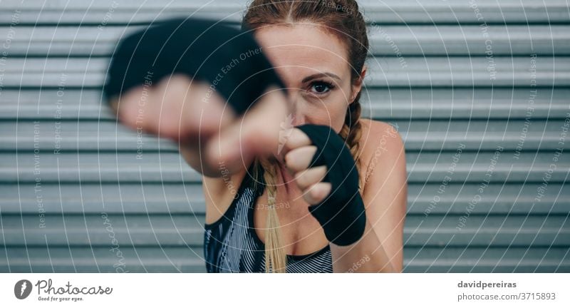 Sportlerin schaut in die Kamera und schlägt stark schauende Kamera schlagend Bowle Boxverband Ermächtigung Metallwand Training Boxerflechten Fitness Körper