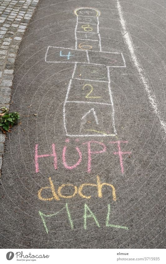 Mal wieder Kind sein - auf dem grauen Asphalt sind mit Kreide Hüpfkästchen aufgemalt und die Aufforderung "Hüpf doch mal" geschrieben Kindheit Spielen Malkreide